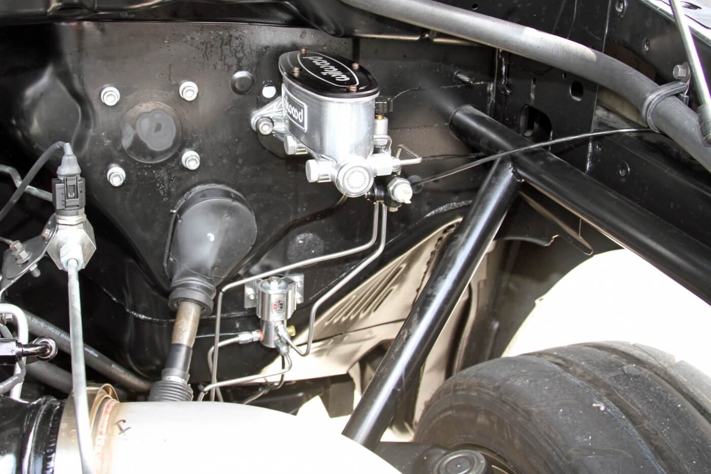 The firewall has been greatly simplified with the factory master cylinder and brake booster removed to make way for the Wilwood master cylinder and Hurst roll control solenoid. You can also see where the roll cage exits the firewall and is tied into the front of the factory frame.