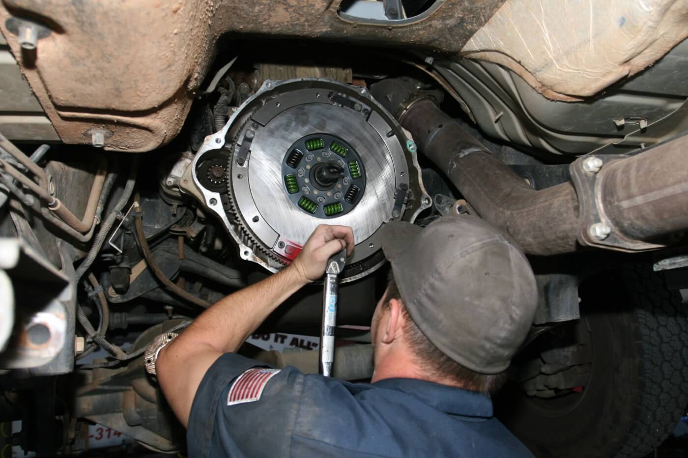 11. The first disc is installed with side marked ”flywheel” against the flywheel, followed by the center plate. The red paint markings made it easy to align the center plate and disc with the flywheel. The alignment tool is used to hold the flywheel disc in alignment with pilot bearing, and 3/16-inch hex Allen bolts slide through the wings of the center plate into the flywheel. The strap is attached to the center plate at the factory, leaving us to attach the other end to the flywheel with TP45 or T45 bolts. Anthony applies red Loctite to all the bolts before tightening them to 24 ft-lb.